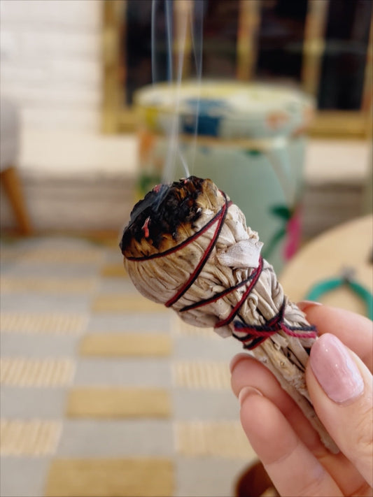 Sage stick in bundle with smoke wafting in front of plaid carpet and floral ottoman and fireplace