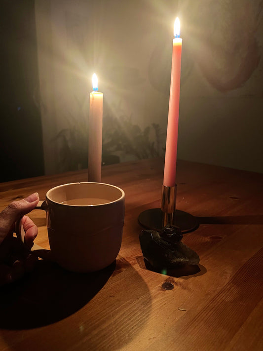 Hand holding mug in candlelit room with pink candles and smoky quartz crystal for relaxing ritual