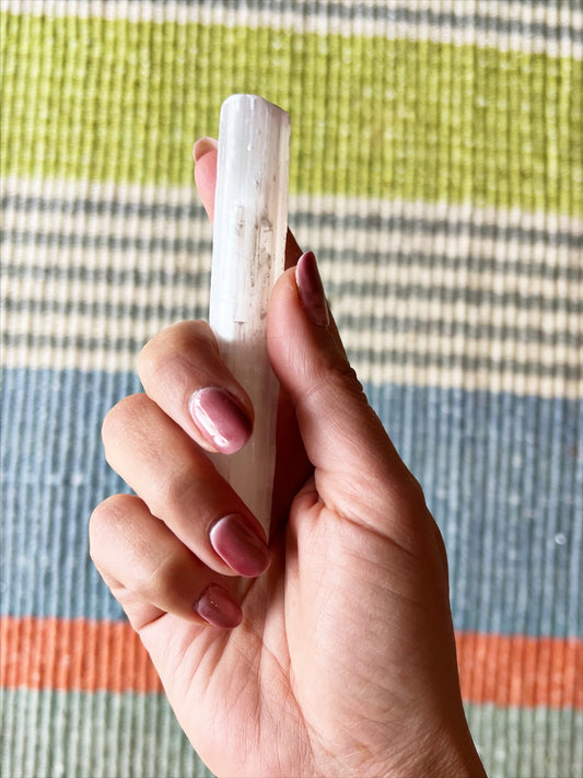 Hand holding large selenite wand over striped green blue and orange rug